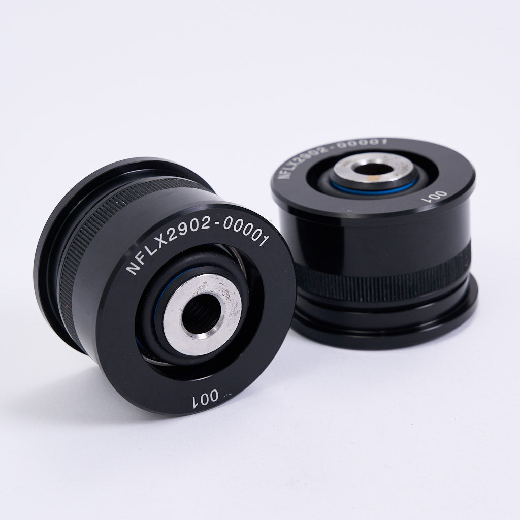 Zwei schwarze zylindrische NoFlex Lager von 55Parts mit metallischen Zentren und eingravierten Codes, konzipiert als Uniballlager für BMW 3er E36/E46, X3 E83, Z4 E85/E86 hinteren Längslenker zur Verbesserung der Fahrdynamik.