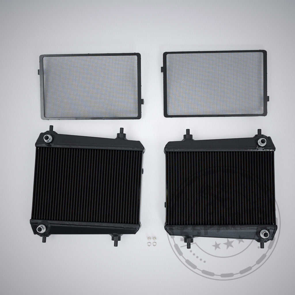 Zwei schwarze 55Parts Aluminium Upgrade Kühlmittelkühler (Wasserkühler seitlich) für BMW G87 M2, G80/G81 M3, G82/G83 M4 S58 plus Netzgitter und Hardware werden nebeneinander auf einer grauen Fläche dargestellt.