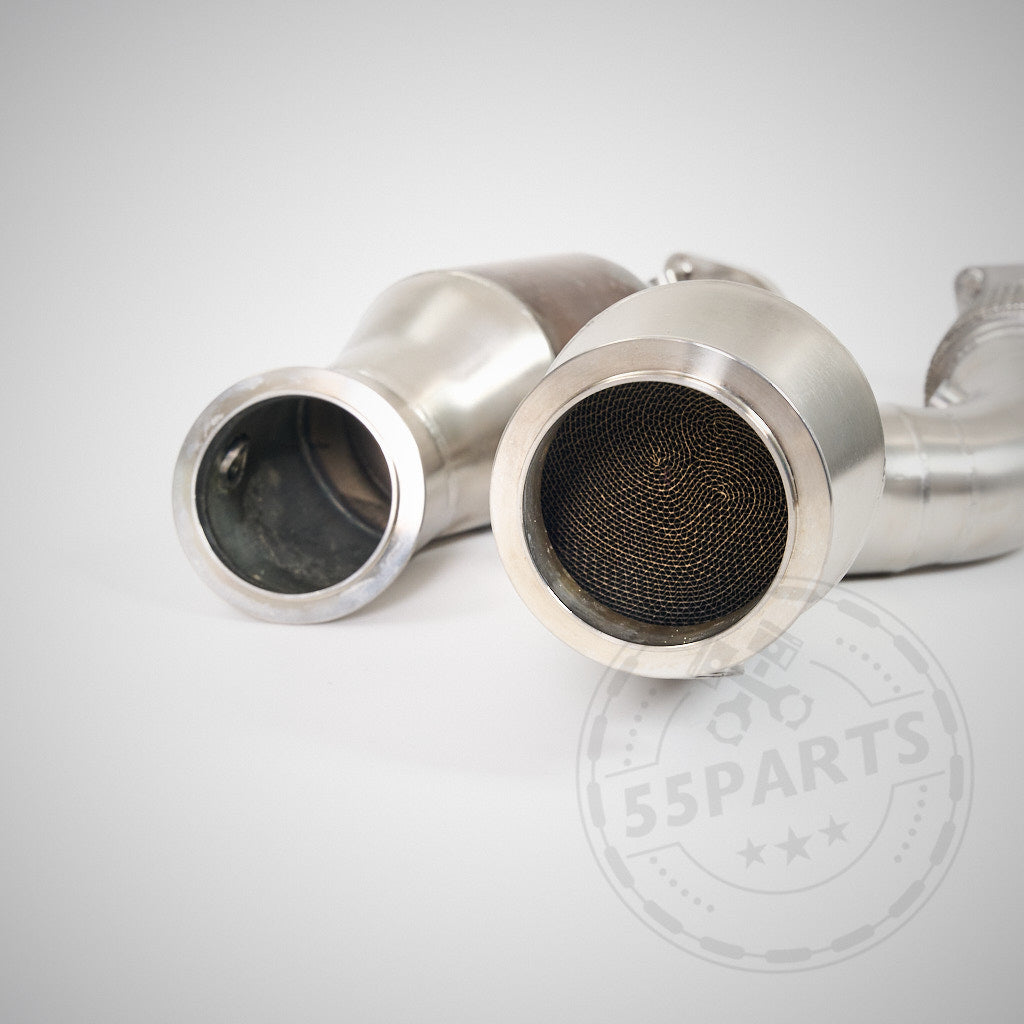 Zwei metallische High Flow Downpipes (mit 200 Zeller Euro 6 Katalysatoren) von 55Parts &amp; MH Pipes, kompatibel mit BMW G87 M2, G80 M3 und G82 M4 S58, sind auf einer weißen Oberfläche abgebildet und verfügen über sichtbare Mesh-Innenseiten für optimalen Durchfluss.