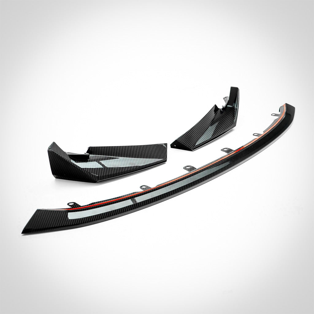 Der Twistnfix TNF+ CSL-Style Frontspoiler Carbon für BMW M3 (G80/G81) & M4 (G82/G83), incl. Teilegutachten, verfügt über ein geschwungenes schwarzes Design mit rotem Akzent in Prepreg-Carbonfaser, dargestellt auf weiß-ideal für die Aufwertung Ihrer Frontpartie.