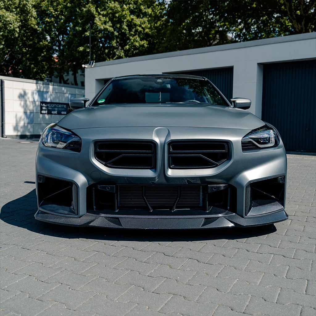 Mattgrauer Sportwagen mit Twistnfix TNF+ Carbon Lufteinlässe passend für BMW M2 (G87) incl. Teilegutachten, mit Performance-Optik und aggressiver Frontstoßstange, geparkt auf einer gepflasterten Auffahrt in der Nähe von Garagen.