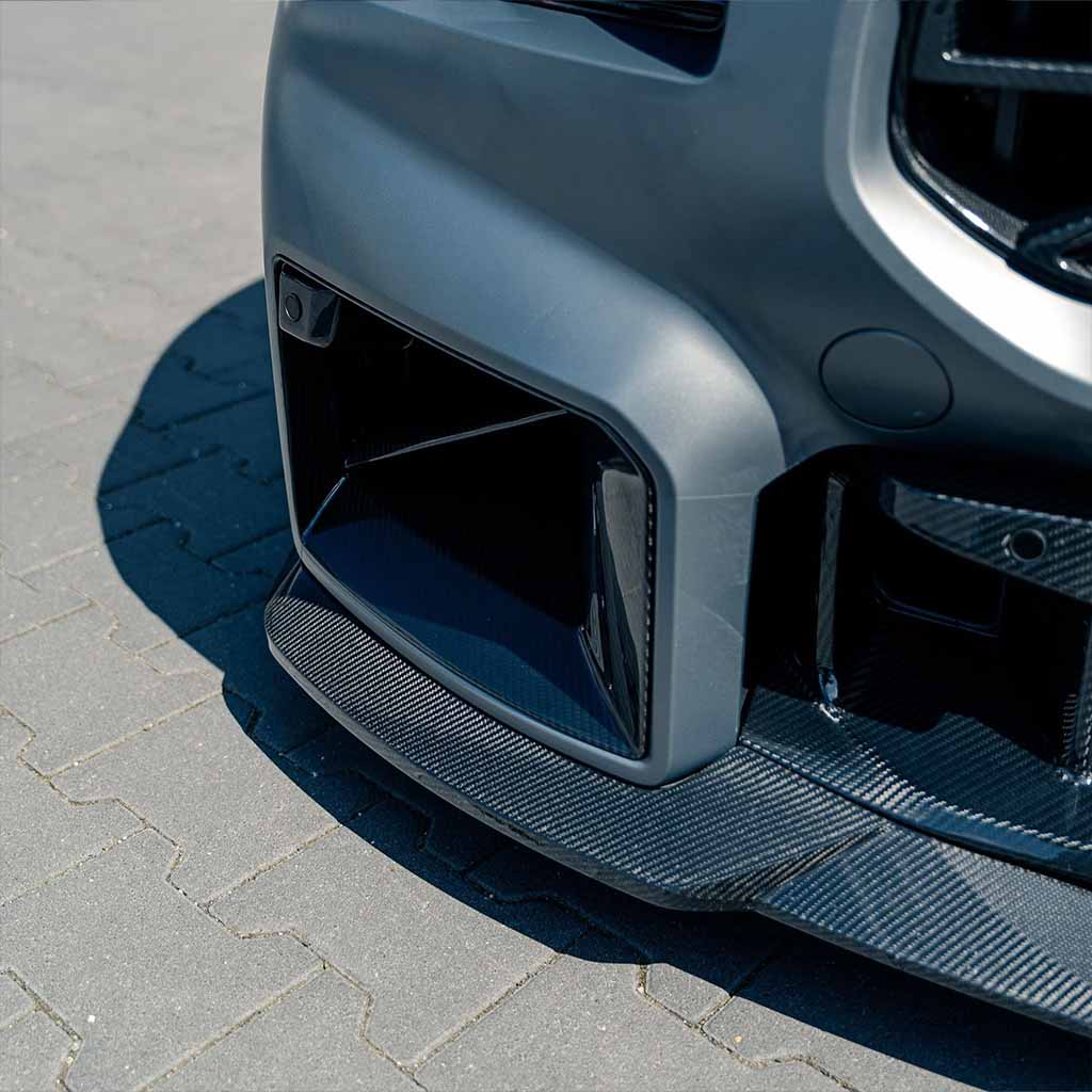 Nahaufnahme von Twistnfix TNF+ Lufteinlässe Carbon für BMW M2 (G87) mit sichtbarer Prepreg-Kohlefaser auf Pflaster - inkl. Teilegutachten für sportliche Performance-Optik.