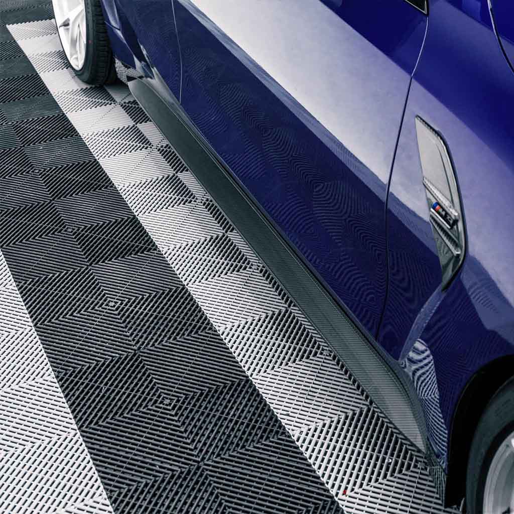 Nahaufnahme des Twistnfix TNF+ OEM-Style Seitenschwellers in Carbon für BMW M4 (G82/G83) inkl. Teilegutachten, abgebildet an einem blauen M4, geparkt auf einem schwarz-weißen geometrischen Boden.