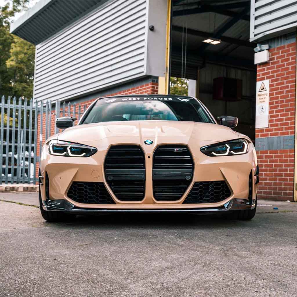 Hellbrauner BMW Sportwagen im CSL-Design vor einer Garage geparkt, mit dem Twistnfix TNF+ Performance Frontspoiler Carbon für BMW M3 (G80/G81) &amp; M4 (G82/G83), inkl. Teilegutachten. Im Hintergrund Metallzäune und Backsteinmauern.