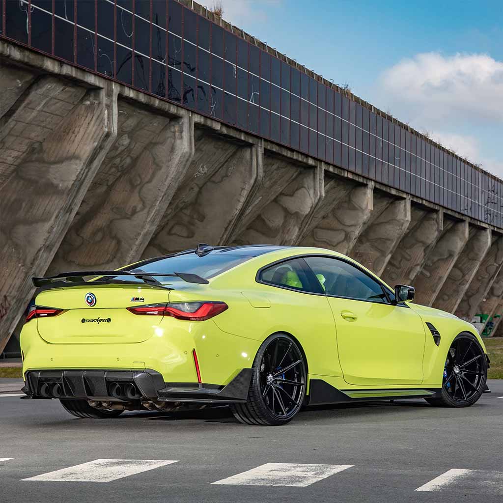 Ein lindgrüner BMW M4 G82 mit Twistnfix TNF+ Performance Seitenschweller Carbon (inkl. Teilegutachten) parkt an einem großen Industriegebäude und unterstreicht seinen sportlichen Look und die eleganten Carbon-Details.