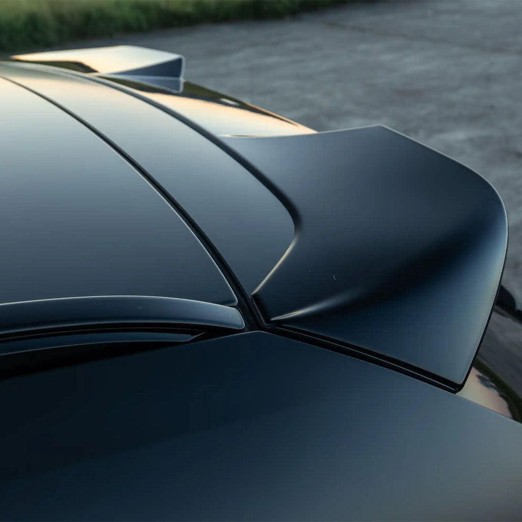 Nahaufnahme eines schwarzen BMW M3 G81 mit ZAERO Design EVO-S Heckspoiler, passend für BMW M3 G81 und G21 von ZAERO, im OEM+ Look vor einem unscharfen Outdoor-Hintergrund.