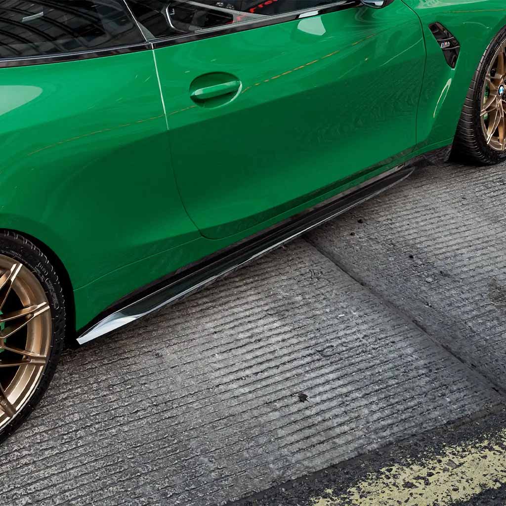 Seitenansicht eines grünen BMW M4 G82 mit ZAERO Design EVO-S Seitenschweller und Bronzerädern, geparkt auf einer Betonstraße.