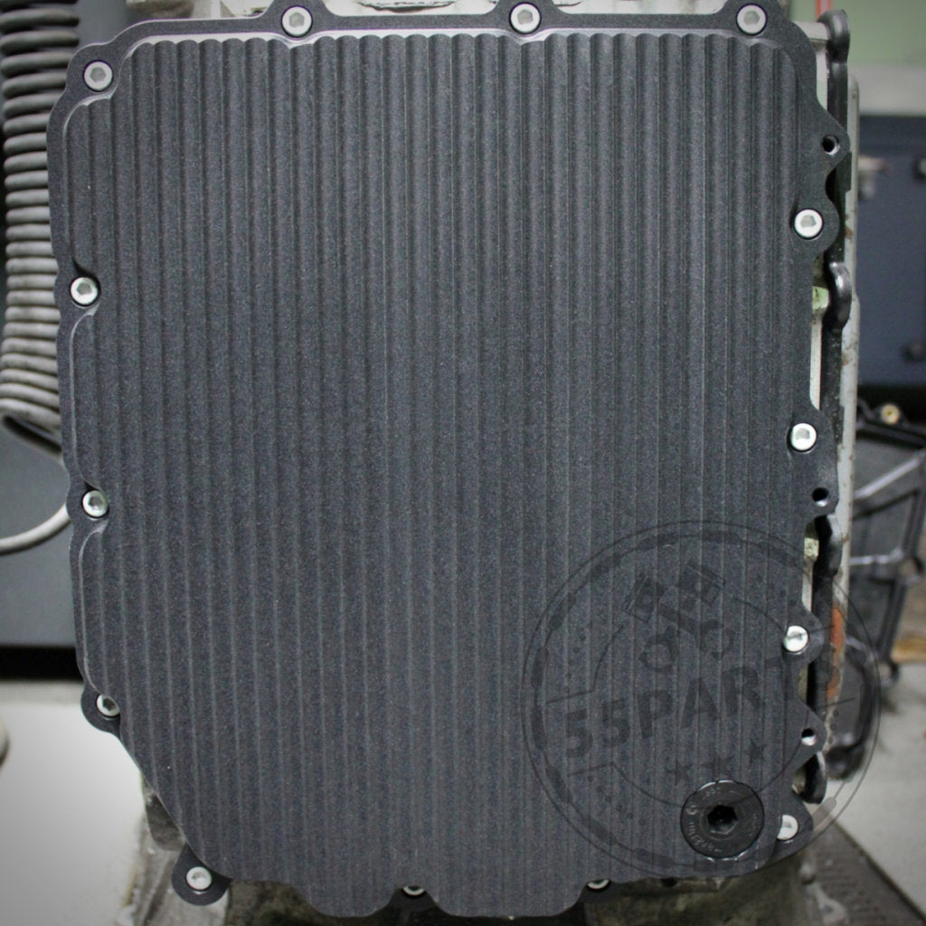 Nahaufnahme einer gerippten, rechteckigen 55Parts Exclusive Aluminium-Ölwanne (DKG GS7D36BG) mit Schrauben am Rand, entworfen passend für BMW 1/335i, M2(c), M3, M4, M5 und M6 E- & F-Serie.