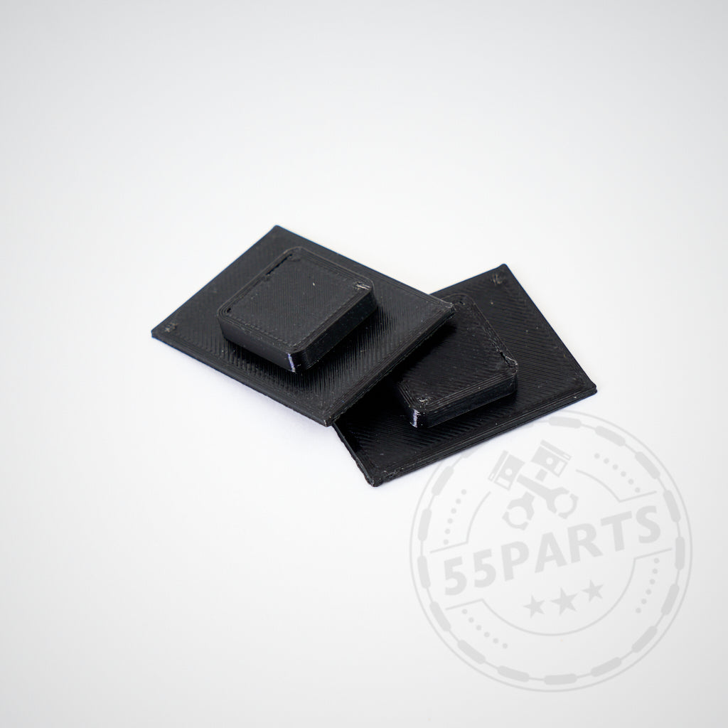 Auf hellgrauem Hintergrund überlappen sich zwei schwarze, rechteckige Kunststoffteile mit erhabenen quadratischen Mittelpunkten. Diese 3D-Druckeinsätze von passen für die Yaris GR Stoßstange mit neuem Kennzeichen.