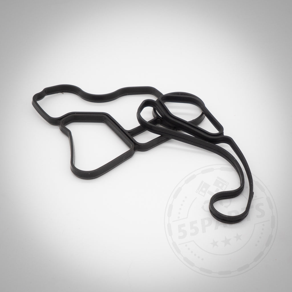 Die 55Parts Dichtung(en) Thermostatgehäuse für N52, N53, N54, N55 und S55 Motoren ist eine schwarze Gummi-Automobildichtung mit unregelmäßiger Form, die auf einem schlichten weißen Hintergrund angezeigt wird.